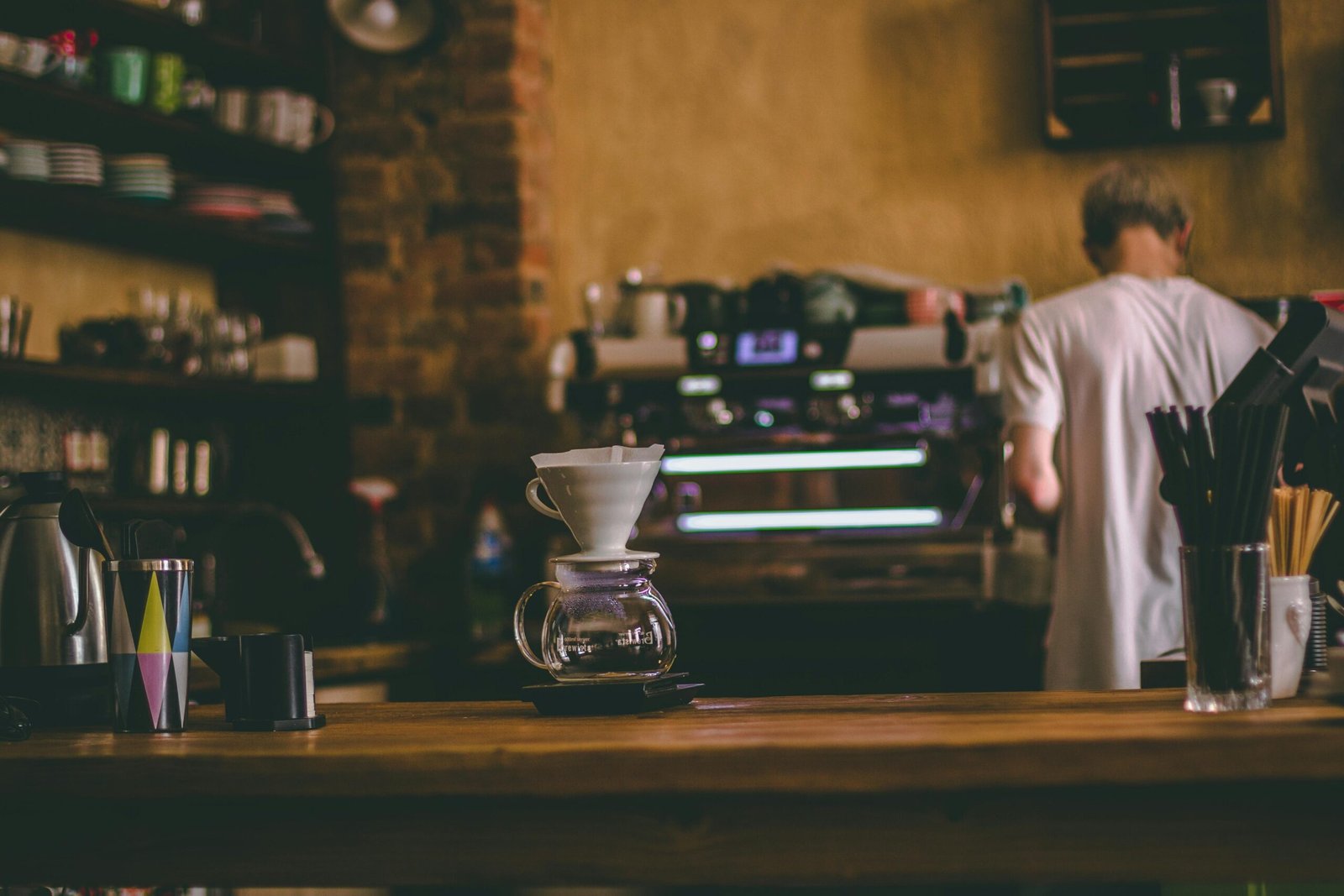 A barista preparing coffee in a cozy café setting with a coffee maker and counter.